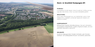 Blick aus einem Flugzeugfenster auf ein Kornfeld mit eingemähtem Minos‑Logo.