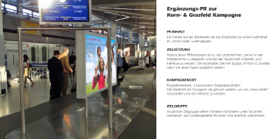 Flughafen‑Gepäckhalle mit Passagieren und Minos‑Werbung auf einem großen Display.